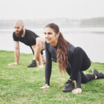 Fitness couple stretching outdoors in park near the water. Young bearded man and woman exercising together in morning